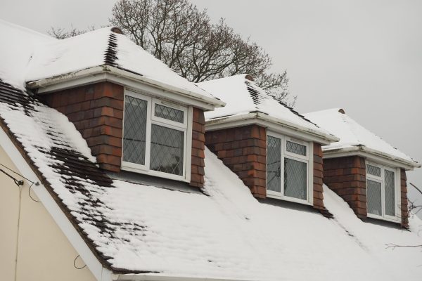 a dormer bungalow roof with the windows of three rooms covered in fresh snow